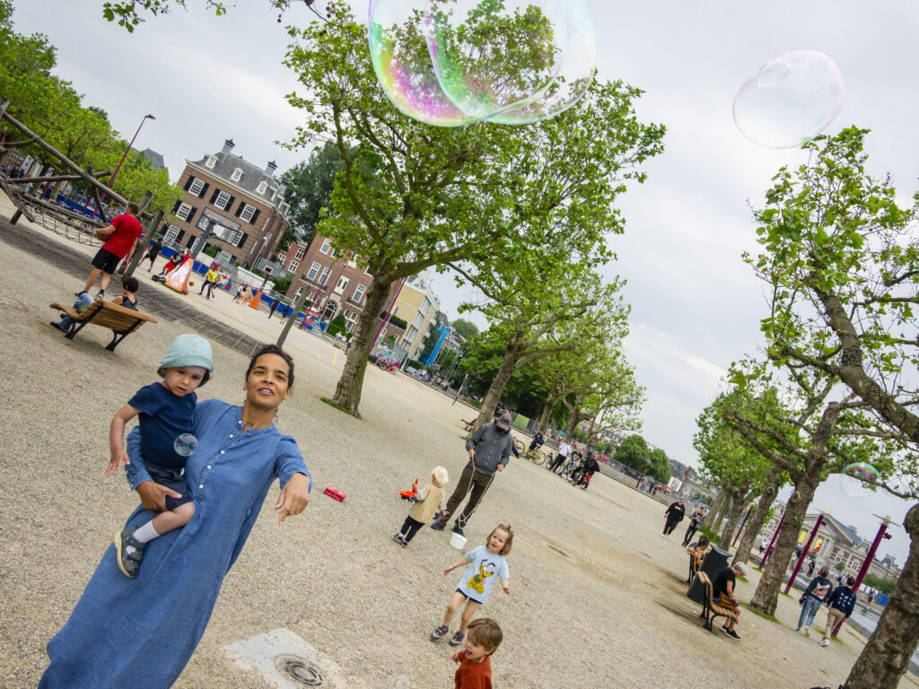 Museumplein Amsterdam, Noord-Holland - dame met kind speelt met zeepballonen - poster A2 door Niek de Greef